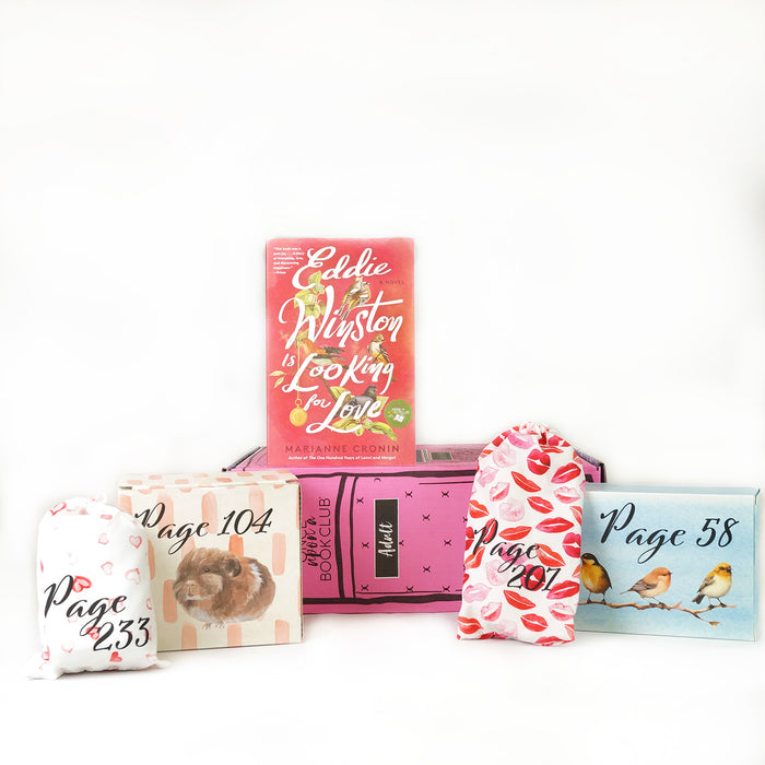 Paperback edition of Eddie Winston is Looking for Love stands on a pink OUABC box. In front of the box are four themed wrapped gifts labeled with page numbers.