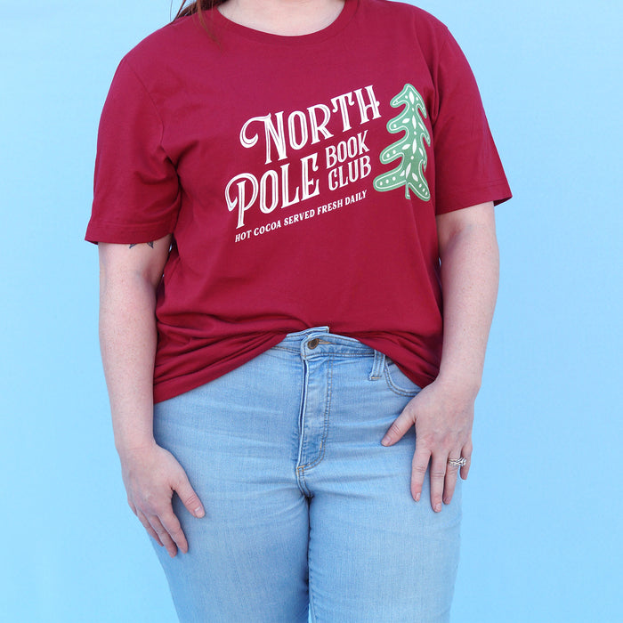 Person wearing a red t-shirt with 'North Pole Book Club' text and graphic on a blue background
