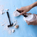 a seashell excavation kit including a compacted seashell filled with seashells, hammer, and brush.