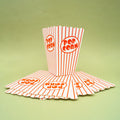 A red and white striped popcorn cup stands on a stack of other flat popcorn cups.