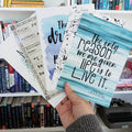 a white hand fans out a set of quote cards in front of a bookshelf