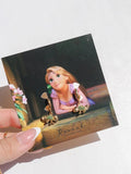Rapunzel Pascal Earrings Tangled-themed on a branded card with a hand holding it.