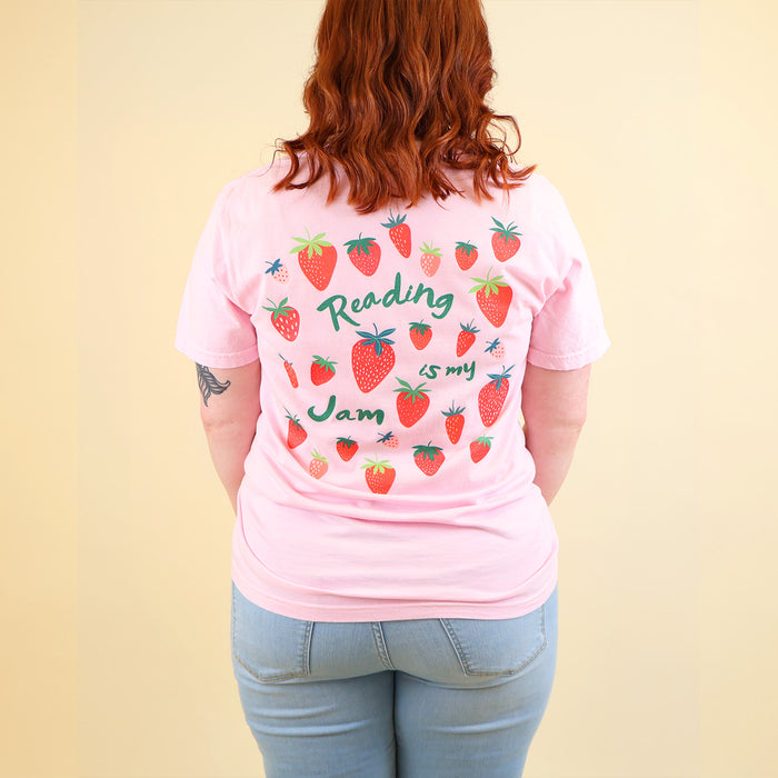 Woman wearing a pink t-shirt with a strawberry designs and text that says 'Reading is my Jam' on a beige background