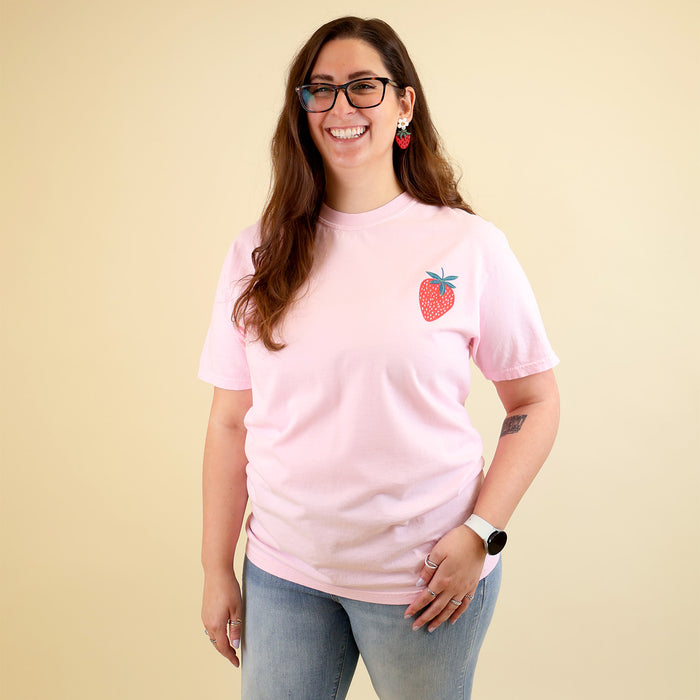 Woman wearing a pink t-shirt with a strawberry designs and text that says 'Reading is my Jam' on a beige background