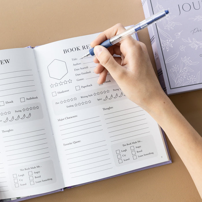 The inside of the reading journal showcasing the book review page details. A hand holds a pen over the page, preparing to write.