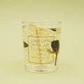 A glass candle votive containing jelly wax, gold glitter, and rose petals. The jar reads "Outlaw King of Flowers" Rose Scented Candle.