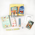 A hardcover copy of The Bookshop of Dust and Dreams by Mindy Thompson sits on a yellow Once Upon a Book Club tween box. This box is surrounded by wrapped gifts labeled with page numbers in addition to paperwork including a signed bookplate from the author, bookmark, activity sheet, and matching collectible sticker.