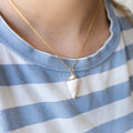 A person wearing a light blue and white striped shirt wears a seashell necklace with a gold chain.