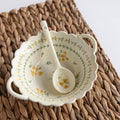 A white ceramic soup bowl with yellow and green floral pattern and a matching spoon.