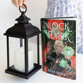 A hardcover edition of Unlock the Dark next to a black lantern with a fake white candle in it.