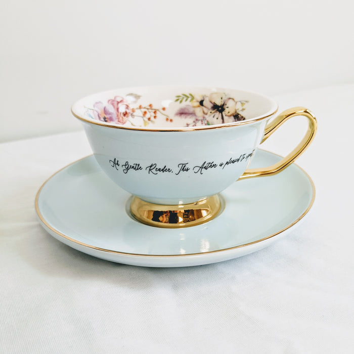a light blue teacup with gold detail and a quote printed on the outside of it with floral details printed on the inside.