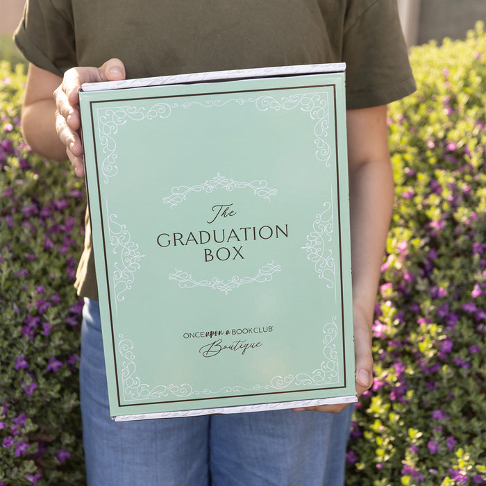 A white woman holds a closed Graduation box outdoors.