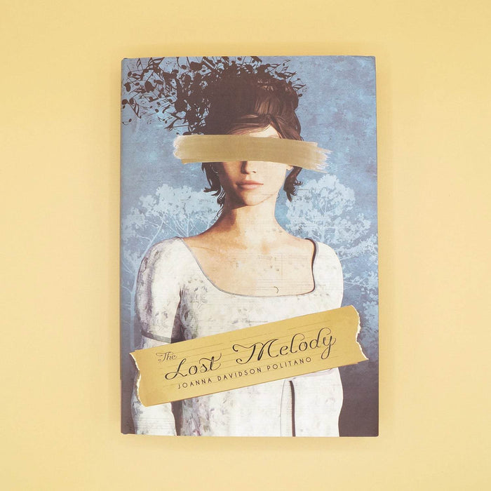The front dustjacket of a hardcover special edition of The Lost Melody. The cover shows a white woman wearing a white dress with a gold brushstroke over her face and her dark hair is floating away in pieces.