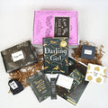 A hardcover edition of Darling Girl leans against a pink box. In front of the box are a black box, black drawstring bag, quote card, bookmark, signature card, bookclub kit, black box, and white and gold envelope. The boxes and envelope all have page numbers on them