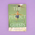 A paperback copy of The Perfect Guests by Emma Rous sits on a purple background