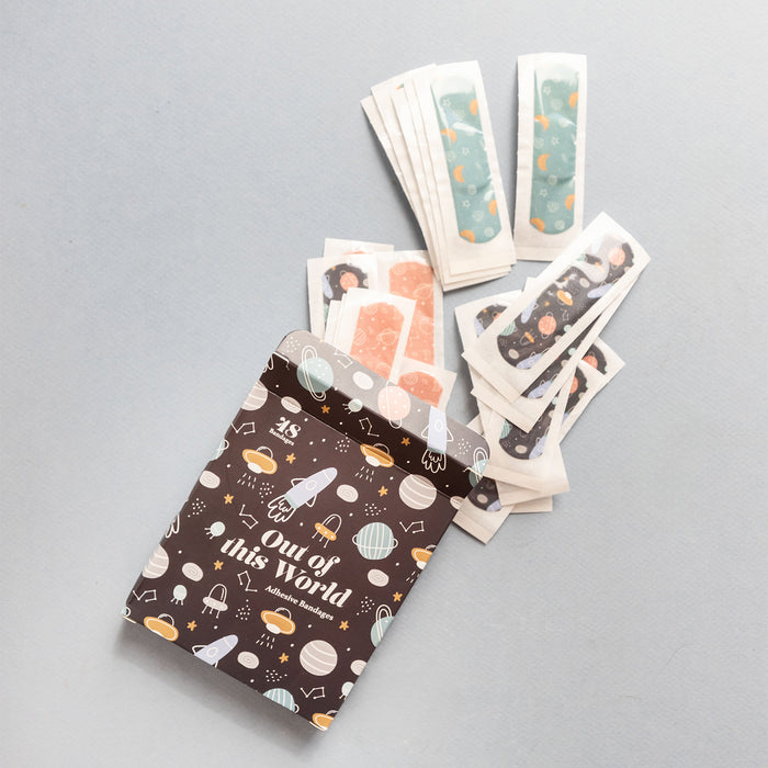 A box with spaceships and planets on it labeled "Out of this World adhesive bandages" has space-themed bandages coming out of the top