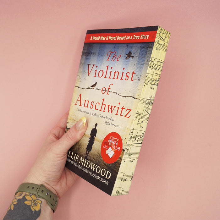 Book titled 'The Violinist of Auschwitz' held by a hand on a pink background