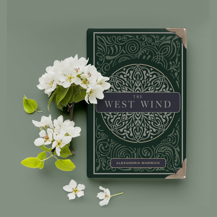 a dark green hardcover special edition of The West Wind with metal corners sits next to white flowers