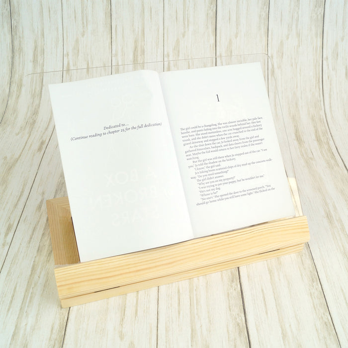 a light wood and plexiglass book stand holds an open book.