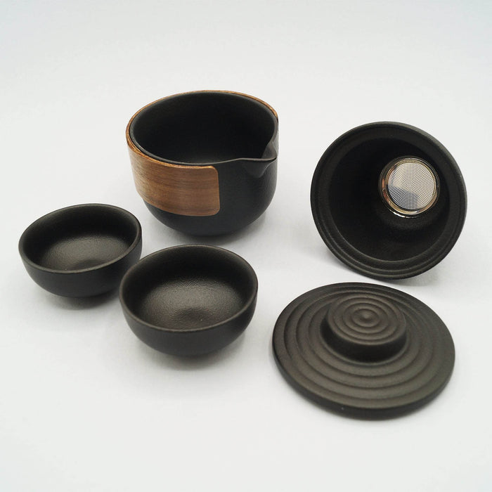 A black ceramic and wood tea set including one tea pot, one tea strainer, one lid, and two small tea cups.
