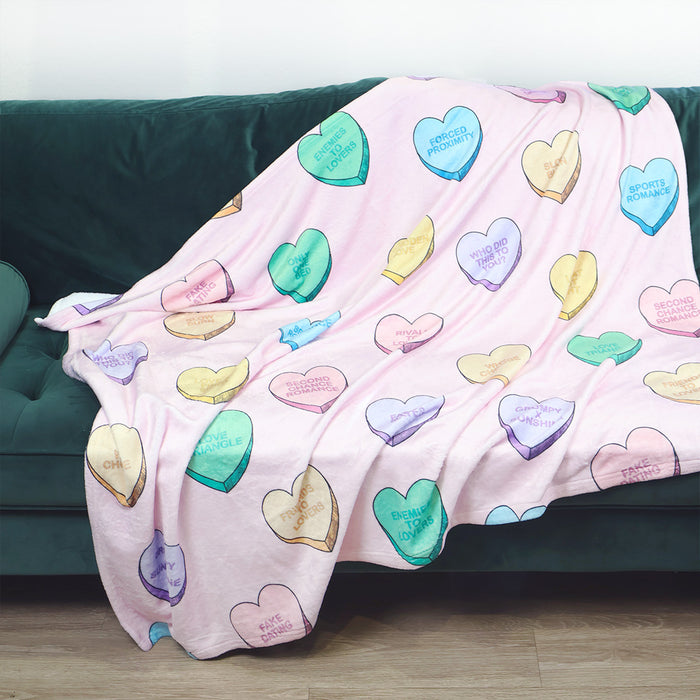 Colorful heart-shaped candy pattern on a pink blanket draped over a green couch.