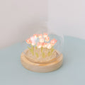 A glass dome with a wooden baseand multiple light-up pink tulips.