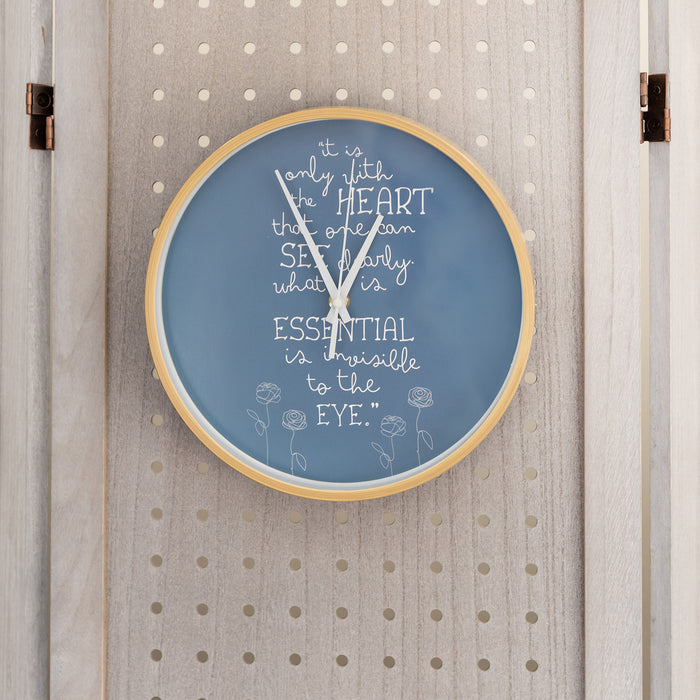 A grey-blue clock face featuring a quote from A Little Prince "It is only with the heart that one can see clearly what is essential is invisible to the eye." and sketches of roses along the bottom of the wood-toned frame.