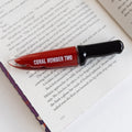 A knife-shaped bottle of red lipstick that says Coral Number Two on the side lays on an open book.