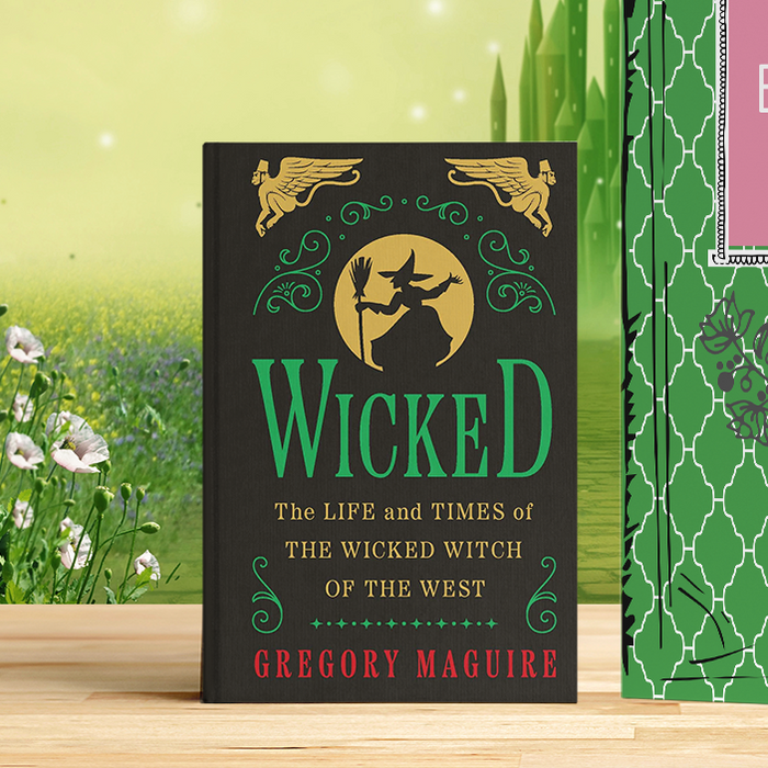 Green book with pink label and black book titled 'Wicked' on a wooden surface with a nature background.