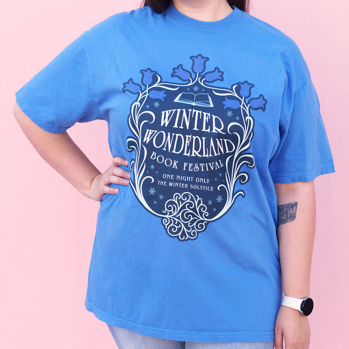 Person wearing a blue t-shirt with 'Winter Wonderland Book Festival' design on a pink background