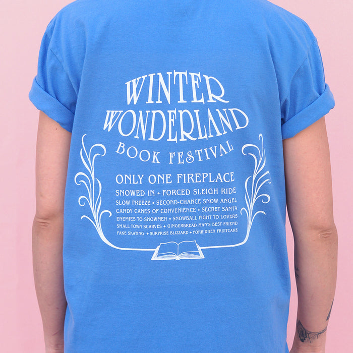 Back of the blue Winter Wonderland Book Festival t-shirt with white text and design on a pink background