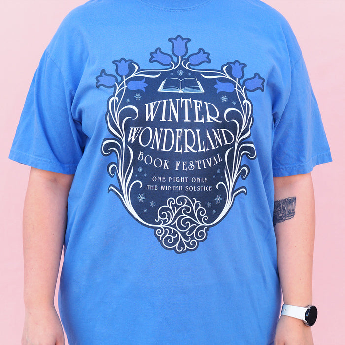 Blue t-shirt with 'Winter Wonderland Book Festival' design on a pink background