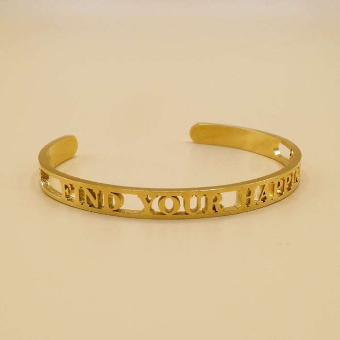 A gold bangle bracelet with the engraved words "FIND YOUR HAPPINESS" displayed against a simple light background.